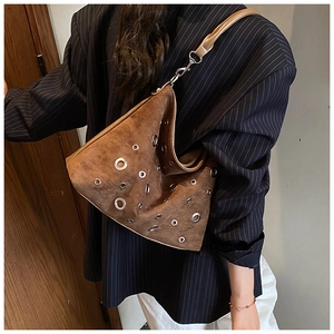 Sac à bandoulière en daim marron avec œillets argentés porté sur un blazer rayé