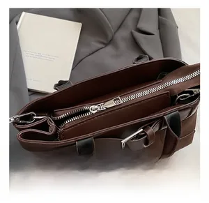 Detail shot of a dark brown matte leather handbag featuring silver metal zippers and buckles