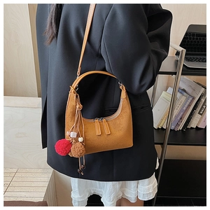 Gros plan du sac sous le bras en daim marron avec un pompon décoratif bicolore