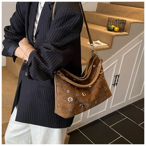 Détail du sac cabas en daim marron foncé avec œillets métalliques argentés et bandoulière