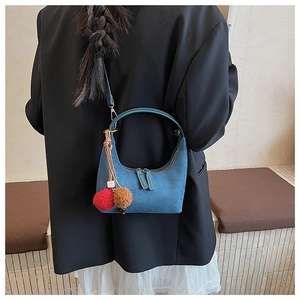Sac hobo en daim bleu avec pompon, présenté de dos par un mannequin en situation
