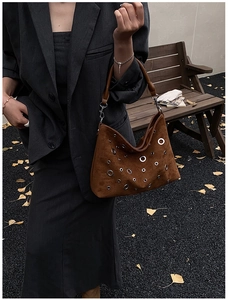 Sac sous le bras en daim marron avec rivets argentés porté sur un blazer gris foncé