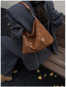 Sac bandoulière en daim marron avec œillets argentés porté par un mannequin en automne