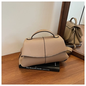 Close-up of khaki pebbled leather shoulder bag with top handle on a stack of books