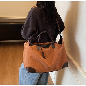 Dettaglio di una borsa tote grande in camoscio marrone con trama e manici in pelle sulla spalla