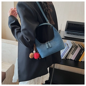 Détail d'un sac demi-lune en daim bleu marine avec double fermeture éclair et pompon coloré