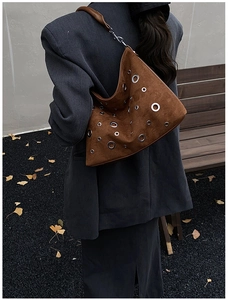 Détail du sac à bandoulière en daim marron avec rivets argentés porté par un mannequin