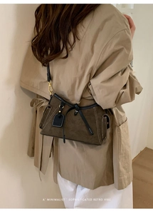 Detail view of olive green suede crossbody bag with gold buckle on beige trench coat