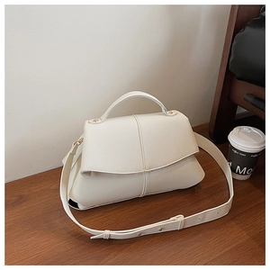 Detail of off-white lychee grain leather shoulder bag with gold hardware on wooden table