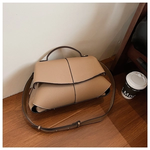 Detail of a brown leather puzzle shoulder bag with geometric stitching on wood
