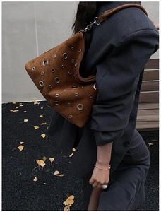 Détail du sac bandoulière en daim marron avec œillets argentés sur costume gris