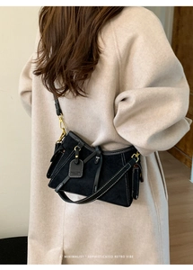 Detail of retro black suede crossbody bag with contrast stitching and gold metal hardware