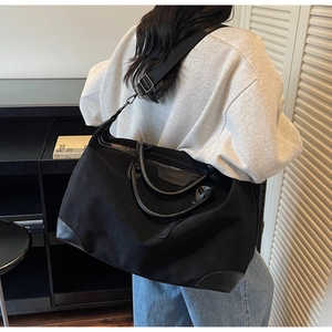 Dettaglio di una grande borsa da viaggio nera con manici in pelle e logo sulla spalla
