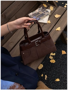 Close-up of vintage dark brown tote bag with buckle detail on a park bench