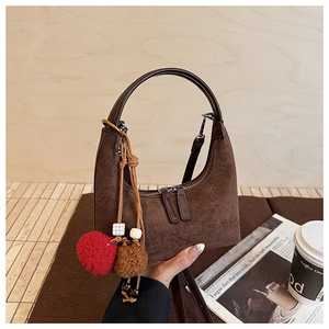 Détail du sac à main en daim marron avec poignée en cuir et pompons en peluche