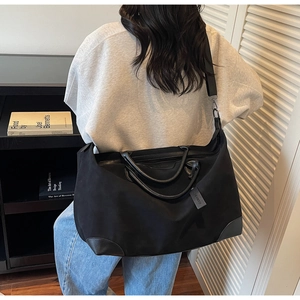 Detailed view of a large black nylon tote bag worn crossbody in a minimalist setting