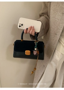 Close-up of black leather crossbody bag with gold buckle and brown floral charm