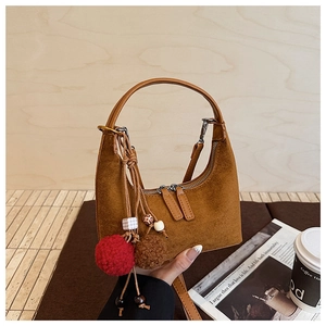 Détail d'un sac hobo en daim marron avec des breloques en peluche et des glands chic