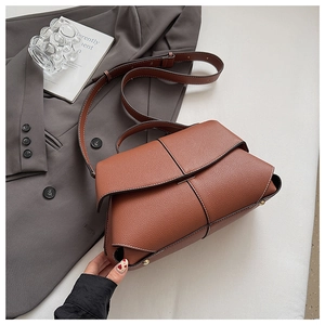 Detail shot of brown lychee grain leather handbag with gold hardware on grey suit jacket