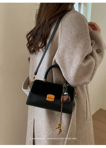 Detail of black leather crossbody bag with gold lock and brown floral charm