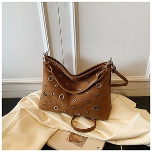 Sac seau en daim marron avec œillets argentés posé sur un magazine, décor lifestyle