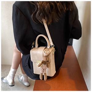 Detail view of beige matte leather crossbody bag with cute bunny charm and metal handle