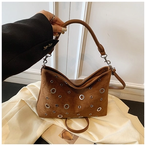 Détail du sac bandoulière en daim marron foncé avec œillets métalliques et style studio
