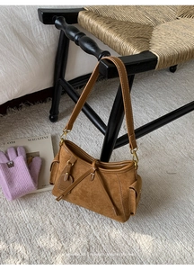 Brown suede tote bag with leather straps and metal charms hanging on a black chair
