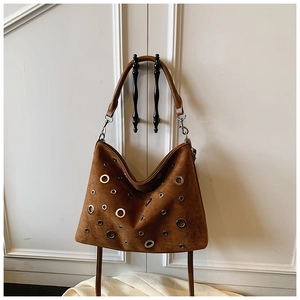Détail du sac hobo en daim marron avec œillets métalliques sur une poignée de porte