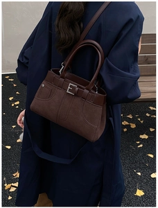 Brown matte handbag with decorative strap details shown on model in outdoor setting