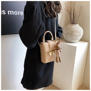 Detail of light beige leather crossbody bag with top handle and cute bunny charm pendant
