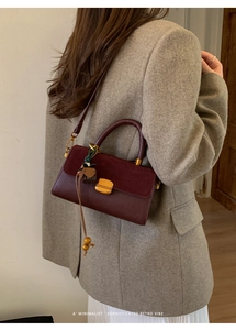 Detail of burgundy retro handbag with gold lock and tassel worn with a gray blazer