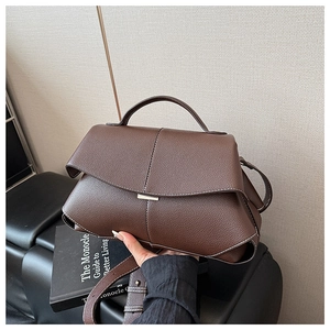 Detail of dark brown litchi leather texture and magnetic metal clasp on a trapezoid bag