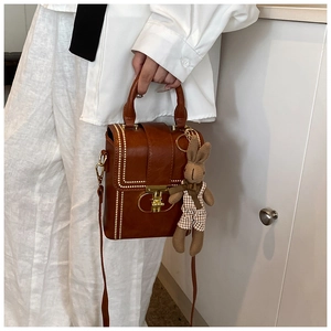 Detail of a brown leather phone bag featuring white stitching and a cute bunny charm