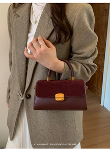 Close-up of burgundy leather handbag featuring a gold buckle and minimalist retro design