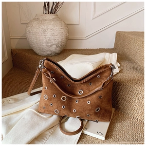 Sac bandoulière en daim marron avec œillets argentés posé sur un manteau blanc