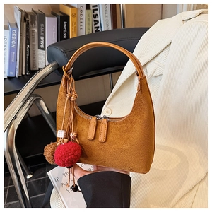 Détail du sac hobo en daim marron avec pompon rouge et fermeture éclair en métal