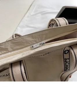 Detail des silbernen Metallreißverschlusses und Markenlogos am beigen Shopper