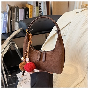 Gros plan du sac hobo en daim marron avec breloque pompon dans un cadre esthétique chaleureux