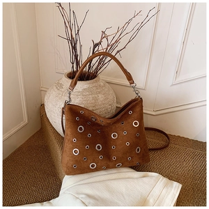 Détail du sac cabas en daim marron avec œillets métalliques sur un tapis tissé