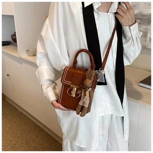 Detail of a brown leather crossbody bag featuring white polka dot stitching and a gold lock