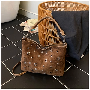Détail du sac seau en daim marron avec œillets métalliques sur sol en carrelage brillant