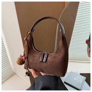 Détail du sac hobo en daim marron foncé avec poignée courbée et pompon décoratif