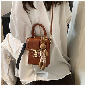 Detail of a brown vintage leather crossbody bag with white bead trim and rabbit charm