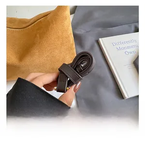 Detail showing adjustable dark brown leather strap with gold hardware on yellow suede bag