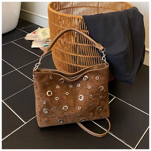 Détail d'un sac en daim marron avec des œillets métalliques argentés et deux bandoulières