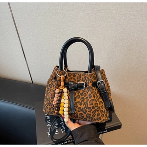 Detail of leopard print bucket bag with beaded charm and black leather handles on books