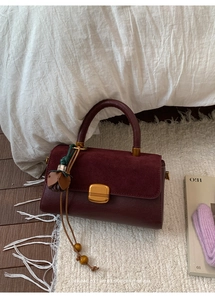 Detail of burgundy flap bag with suede texture, gold buckle and wood bead tassel charm