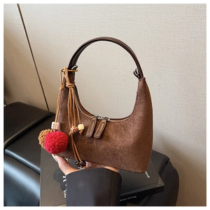 Gros plan du sac hobo en daim marron avec pompons bohèmes sur un livre noir