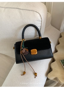 Detail of retro black leather and suede bag with gold buckle and floral pendant charm